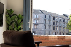 A room with a brown leather chair, a potted plant, and a view of a brick wall and buildings.