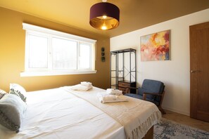 A bedroom with a bed, a chair, a window, a door, and a painting on the wall.