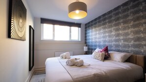 Ein Hotelzimmer mit einem großen Bett, einem Fenster mit Jalousien, einem Wandbild und einer Deckenleuchte.