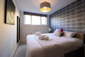 A hotel room with a large bed, a window with blinds, a wall-mounted artwork, and a ceiling light fixture.