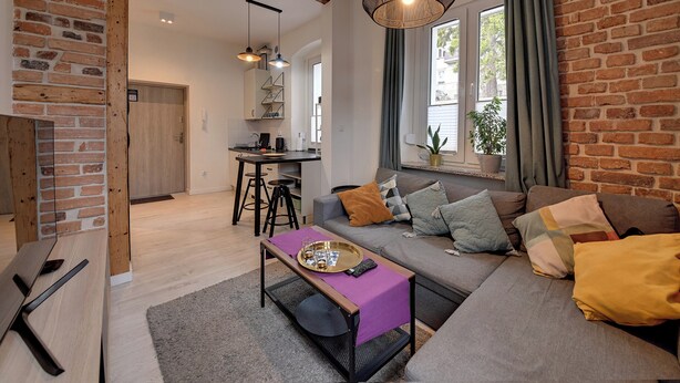 A modern living room with a sofa, a coffee table, and a dining area with a table and chairs. - RentPlanet - Apartament Sikorskiego (Szklarska Poręba)