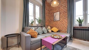 A living room with a grey sofa, a small side table, a coffee table with a tray, a hanging light fixture, and a brick wall. - RentPlanet - Apartament Sikorskiego (Szklarska Poręba)