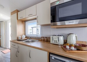A compact kitchen with a microwave, toaster, sink, and a kettle. - Bronze 2 Bedroom Caravan, Sleeps 4 (Great Yarmouth)