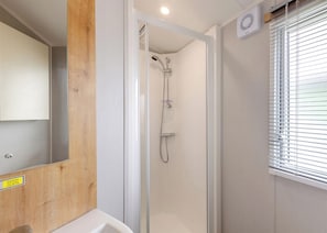 Eine Dusche mit Glastür, Spiegel und einem Fenster mit Jalousien.