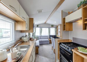 A compact RV interior with a kitchenette, a dining area, a seating area, and a small living space. - Bronze 2 Bedroom Caravan, Sleeps 4 (Great Yarmouth)