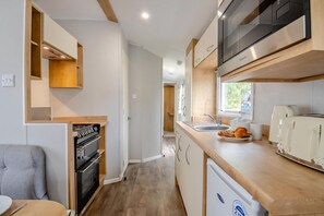 Een kleine keuken met ingebouwde apparatuur, een eethoek met een stoel en uitzicht op de omgeving.