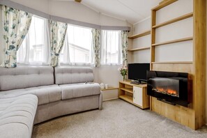 Een woonkamer met een bank, een flatscreen televisie, een open haard en een raam met gordijnen.