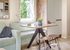 Una sala de estar moderna con un sofá, una mesa de comedor con dos taburetes, una planta en maceta y una ventana con cortinas.