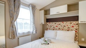 Een hotelkamer met een bed, een raam met gordijnen, een radiator, een hoofdeinde met een patroon en ingebouwde kastjes.
