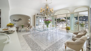 A spacious living area with a glass-top dining table surrounded by chairs, a chandelier, and a view of the city. - Villa Isea Positano (Positano)