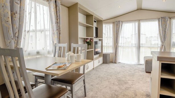 A modern room with a dining table, chairs, a bookshelf, and a TV. - Gold Caravan with parking & decking (Great Yarmouth)