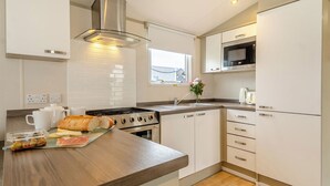 A modern kitchen with a central island, stainless steel appliances, and a window with a view. - Gold Caravan with parking & decking (Great Yarmouth)