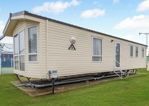 A mobile home with a single window on the side, a door, and a small attached structure with a hose. - Gold Caravan with parking & decking P (Great Yarmouth)