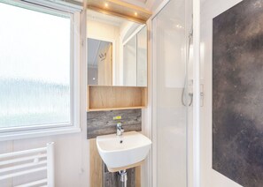 Un baño con un lavabo blanco, estantes de madera, un espejo y una ducha.