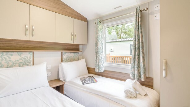 Un dormitorio con dos camas, cabecero de madera, una ventana con cortinas y vistas a un balcón.