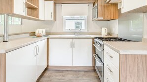 Una cocina compacta con armarios blancos, estufa a gas, microondas y ventana sobre el fregadero.