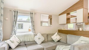 Una sala acogedora con un conjunto de sofás, una mesa de comedor con platos y tazas, y una zona de cocina con armarios y un espejo.