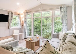 Ein gemütliches Zimmer mit einer Couch, einem kleinen Tisch mit Teekanne und Teller sowie einem Fenster mit Vorhängen.