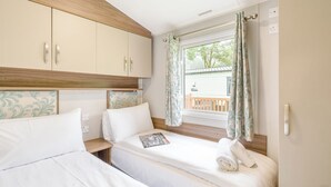 Ein Schlafzimmer mit zwei Betten, einem Holzkopfende, einem Fenster mit Vorhängen und einem Blick auf einen Balkon.
