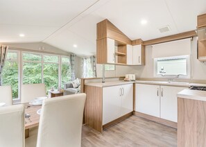A modern kitchen with white cabinets, a wooden countertop, and a window overlooking greenery. - Gold Premium Caravan with ensuite & decking (Great Yarmouth)