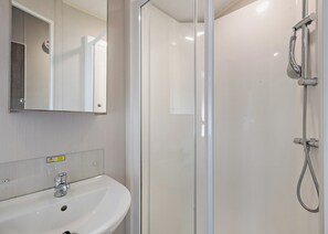 A bathroom with a glass shower enclosure, a white sink, and a mirror. - Silver Caravan with decking 6 (Great Yarmouth)