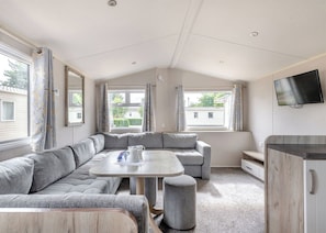 Ein modernes Wohnmobil-Interieur mit einer Eckcouch, einem runden Tisch und einem an der Wand befestigten Fernseher.