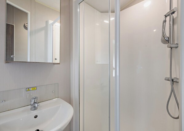 A bathroom with a glass shower enclosure, a white sink, and a mirror. - Silver Caravan with ensuite (Great Yarmouth)