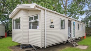 A mobile home with a front porch, a small attached garage, and a visible water meter. - Silver Caravan with ensuite P (Great Yarmouth)