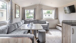 Een modern interieur van een camper, met een hoekbank, een ronde tafel en een aan de muur bevestigde televisie.