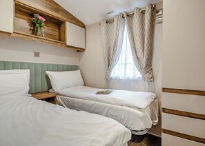 Ein Zimmer mit zwei Betten, einem hölzernen Regal mit einer Vase und einem Fenster mit Vorhängen.