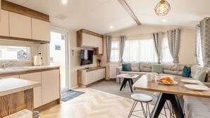 Una cucina moderna con forno a incasso, un'area pranzo con tavolo in legno e sgabelli da bar, un divano e una TV montata a parete.