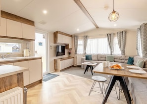 Eine moderne Küche mit Einbauofen, eine Essecke mit Holztisch und Barhocker, ein Sofa und ein an der Wand befestigter Fernseher.