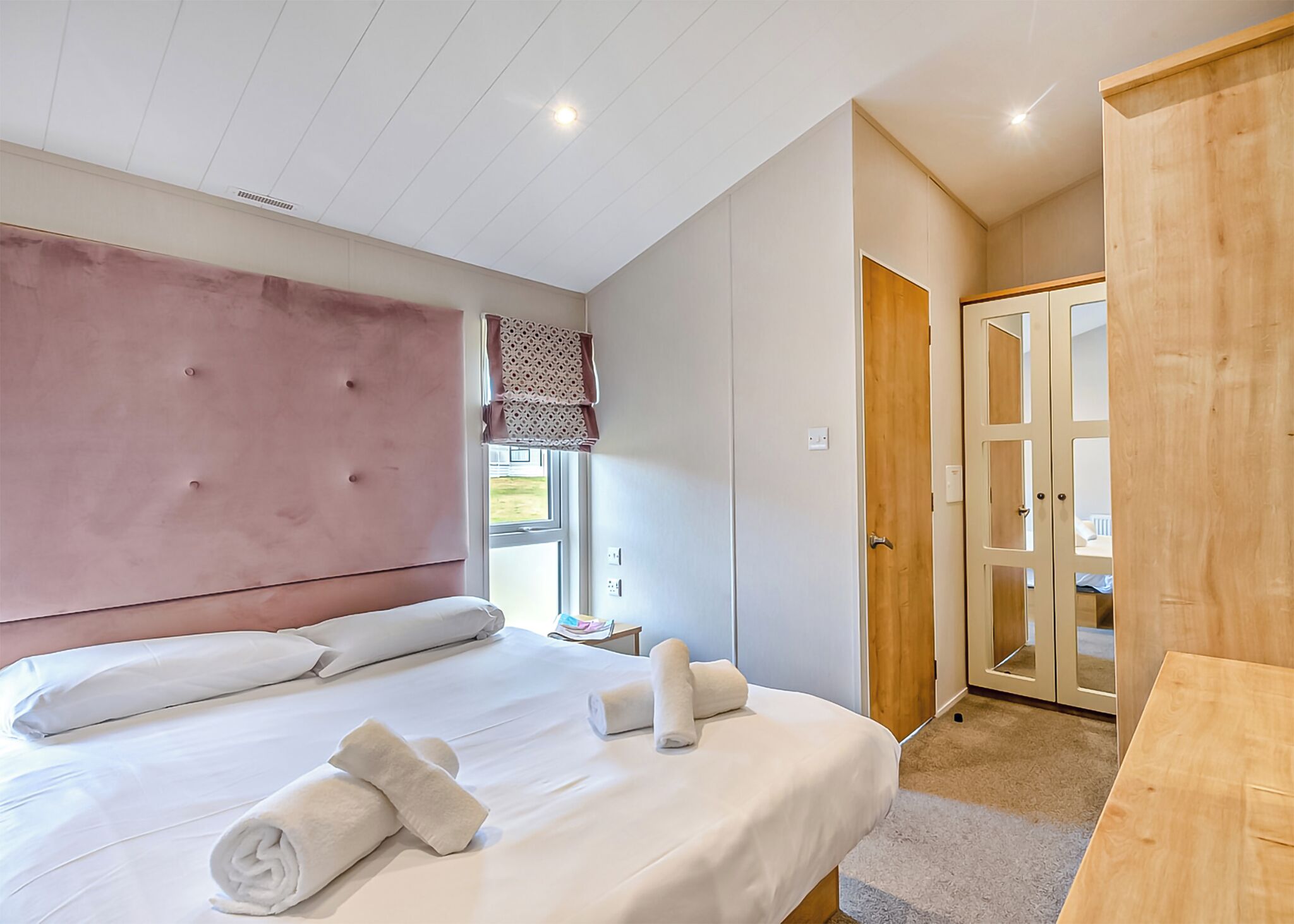 Un dormitorio con una cama grande, un armario de madera, una ventana con vistas y una puerta que da a otra habitación.