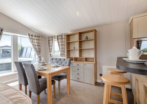 Een moderne keuken met een eettafel, stoelen, een ingebouwde houten plank en een klein barretje.