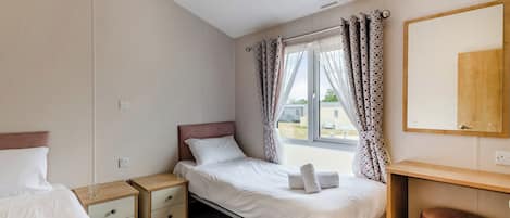 A bedroom with a single bed, bedside tables, a wooden desk, a mirror, and a window with curtains.