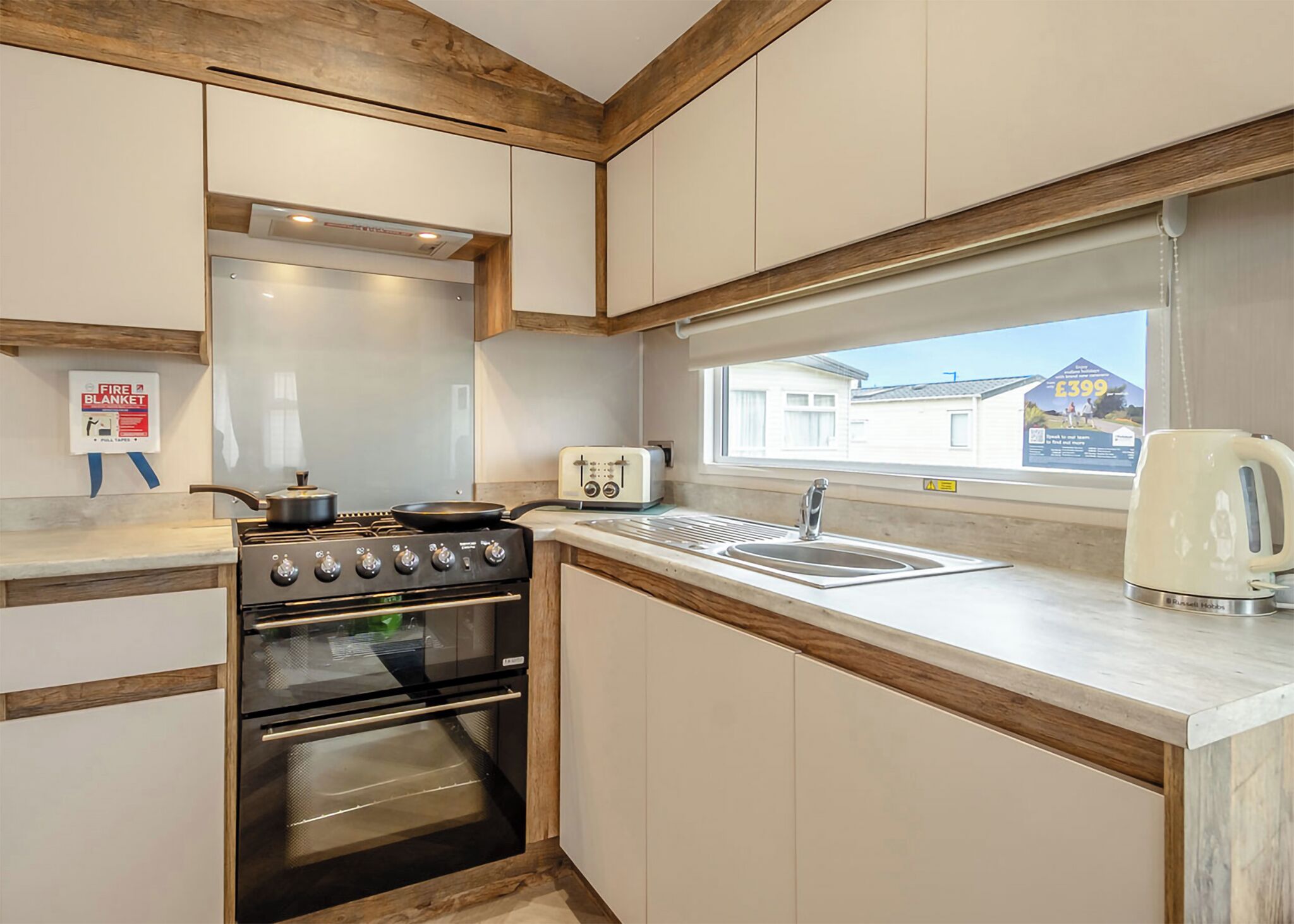A kitchen with a stove, oven, sink, and window with a view of a house.