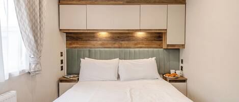 Une chambre à coucher avec un lit, deux tables de chevet, une tête de lit en bois et une fenêtre avec des rideaux.
