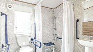 Baño con inodoro, ducha y lavamanos, equipado con barras de apoyo y un banco accesible en silla de ruedas.