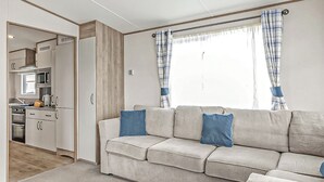 Una sala de estar con sofá, una zona de cocina y un ventanal con cortinas.