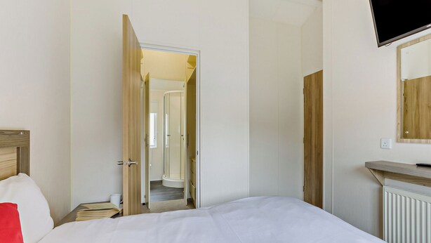 Een slaapkamer met een bed, een aan de muur bevestigde televisie, een houten hoofdeinde en een badkamer zichtbaar door een geopende deur.