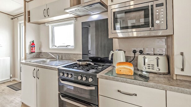 A compact kitchen with a gas stove, oven, microwave, toaster, and a window above the sink. - Gold Accessible with parking P (Great Yarmouth)