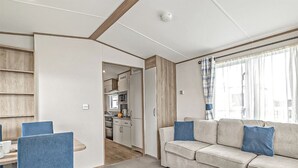 A compact living space with a kitchenette, a sofa with blue cushions, and a dining area with chairs. - Gold Accessible with parking P (Great Yarmouth)