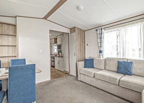 Ein kompakter Wohnbereich mit einer Küchenzeile, einem Sofa mit blauen Kissen und einem Essbereich mit Stühlen.