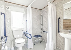 Ein Badezimmer mit Toilette, Dusche und Waschbecken, ausgestattet mit Haltegriffen und einer rollstuhlgerechten Sitzbank.