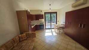 Ein Zimmer mit einer Couch, einem Esstisch, einer Küchenzeile und einer Glastür, die zu einem Außenbereich führt.