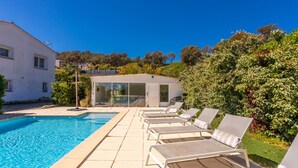 En swimmingpool med liggestole, et moderne hus og en have.