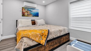 Ein Schlafzimmer mit einem Bett, einem Gemälde, einer Klimaanlage und einem Fenster mit Jalousien.