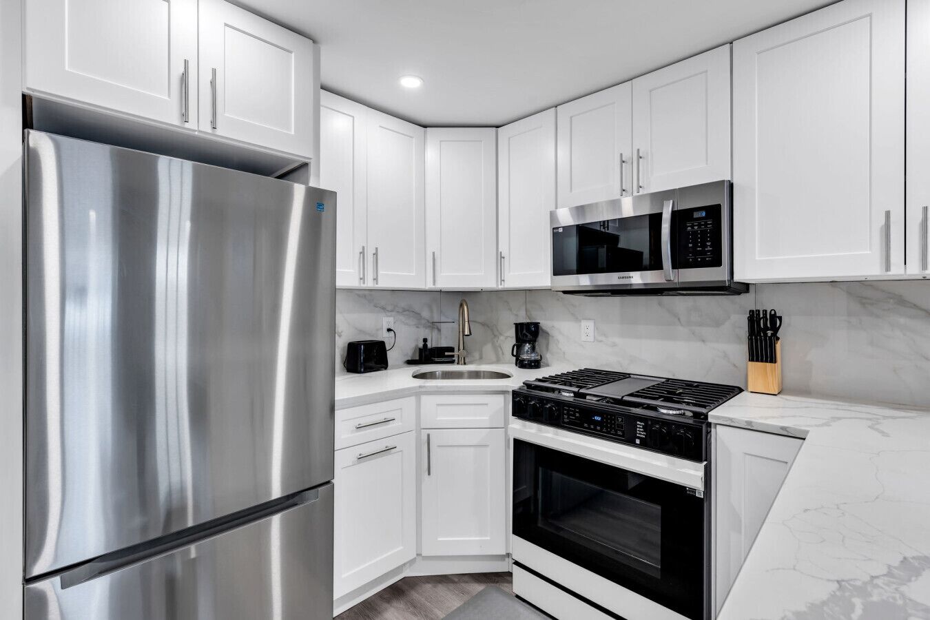 A modern kitchen with white cabinets, stainless steel appliances, a built-in oven, and a microwave.