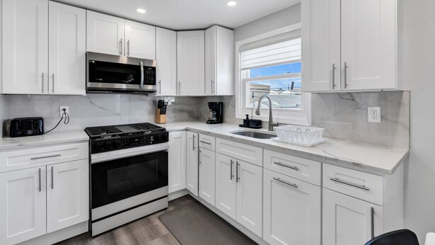 A modern kitchen with white cabinetry, a built-in microwave, a stove, and a window with a view. - Charming Seaside Escape | 2BR, Parking, Beach (Seaside Heights)