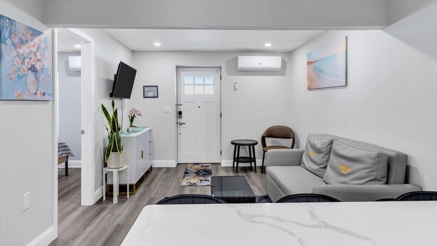 Ein modernes Hotelzimmer mit Bett, einer Couch, einem kleinen Tisch, einem Fernseher, einem Schreibtisch mit Stuhl, einer Topfpflanze und Bildern an den Wänden.